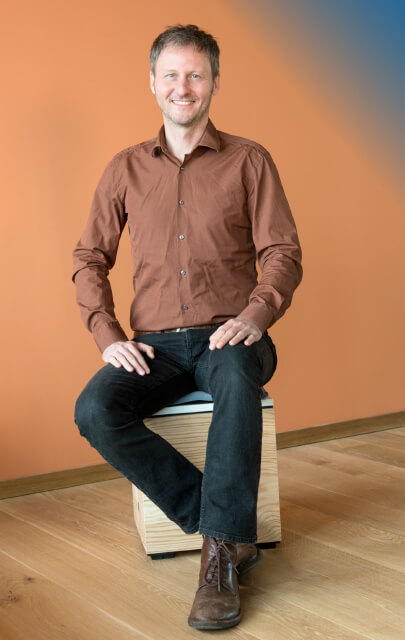 Lars Horstmann vor orangem Hintergrund auf Holzhocker