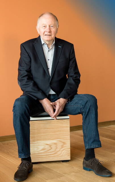 Hans-Werner Horstmann vor orangem Hintergrund auf Holzhocker